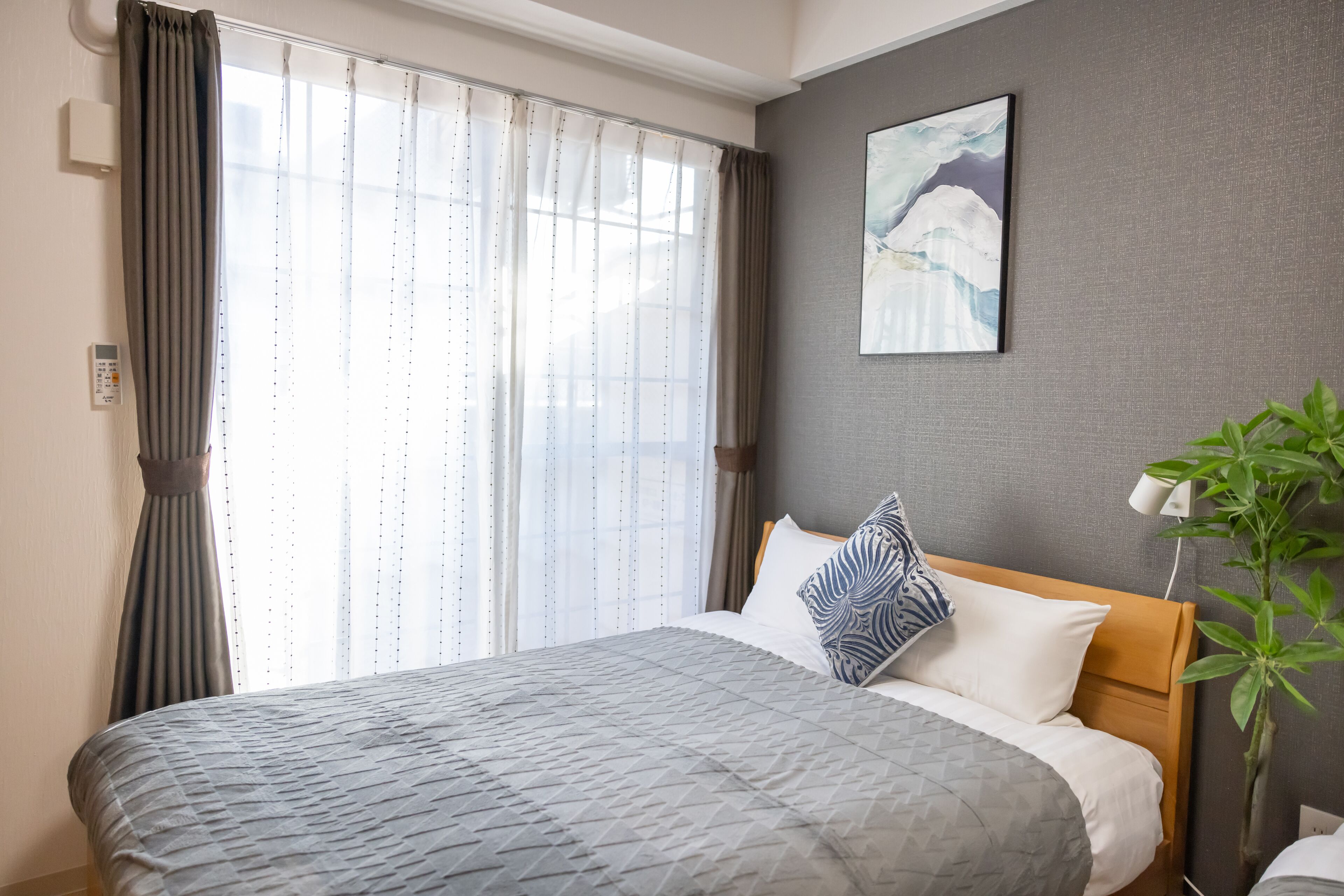 A neatly made bed with a patterned bedspread, a pillow with a blue and white design, and a wall-mounted painting.