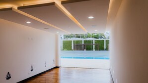 A corridor with wooden flooring and white walls, leading to a pool area with a view of greenery. - Corporate stays Urban flats (Pozos)