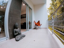 Fachada de un edificio moderno con una estatua, una silla plegable y un balcón con barandilla.