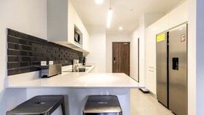 A modern kitchen with a white countertop, black backsplash, stainless steel appliances, and two black bar stools. - Corporate stays Urban flats (Pozos)