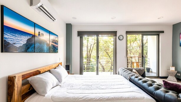 A bedroom with a large bed, a sofa, and a view of the outdoors through a sliding door. - Corporate stays Urban flats (Pozos)