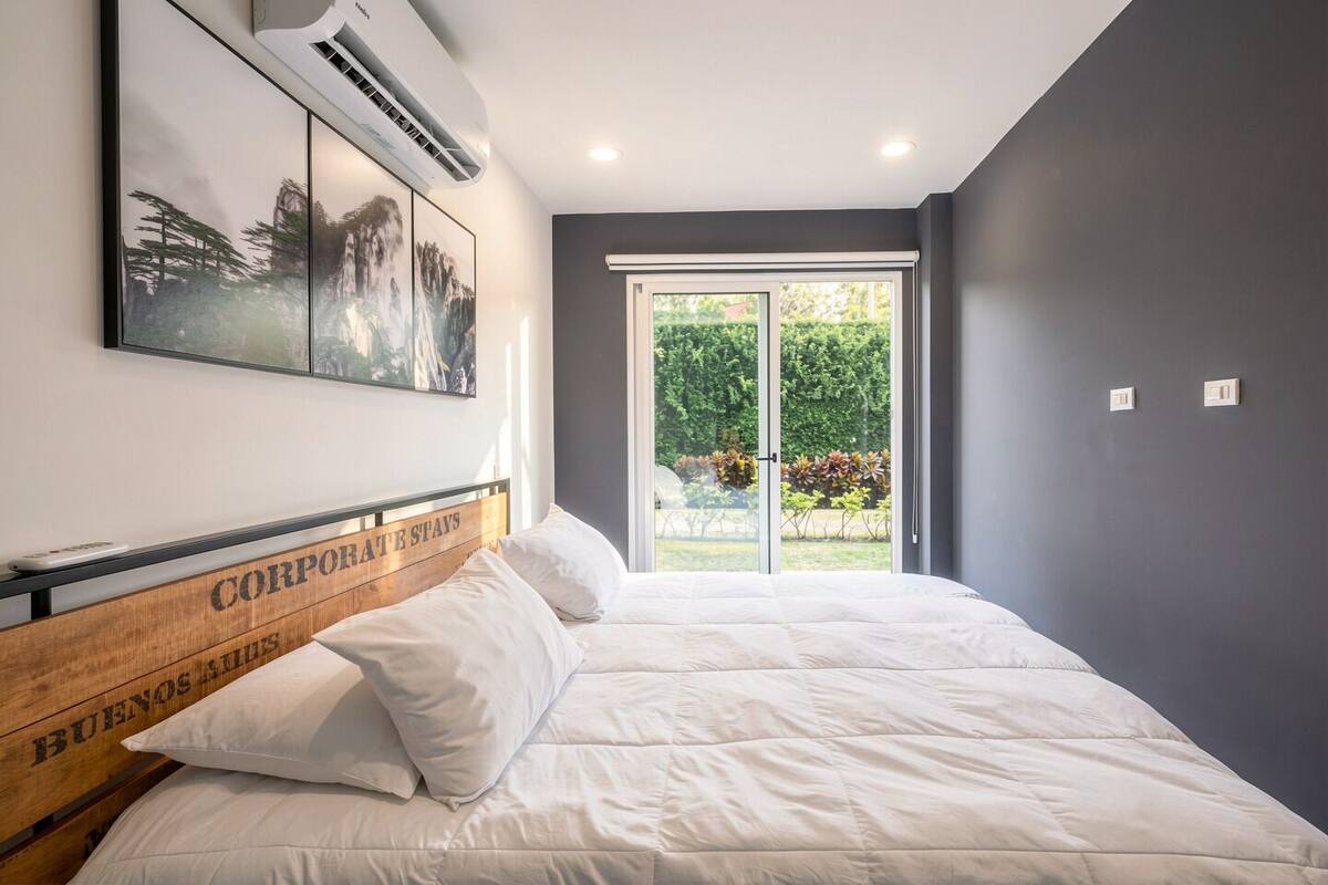 Un dormitorio con cama, aire acondicionado instalado y ventana con vistas a zonas verdes.