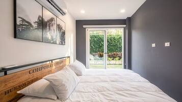 A bedroom with a bed, a mounted air conditioner, and a window with a view of greenery.