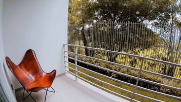 Un balcón con barandilla blanca, un sillón de cuero marrón y vistas a árboles y una cerca.