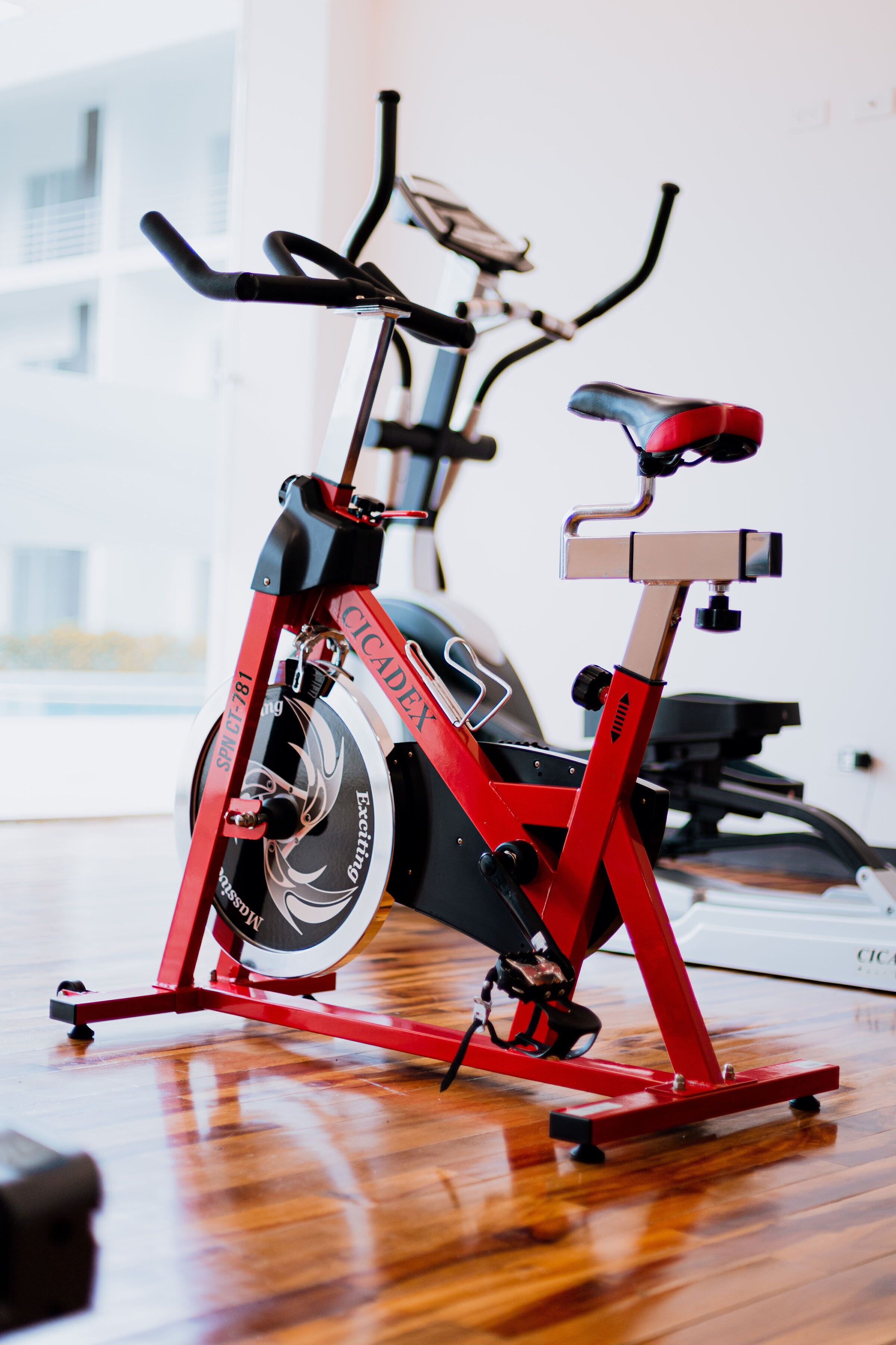 A stationary exercise bike with a red frame and black seat, positioned indoors on a wooden floor.