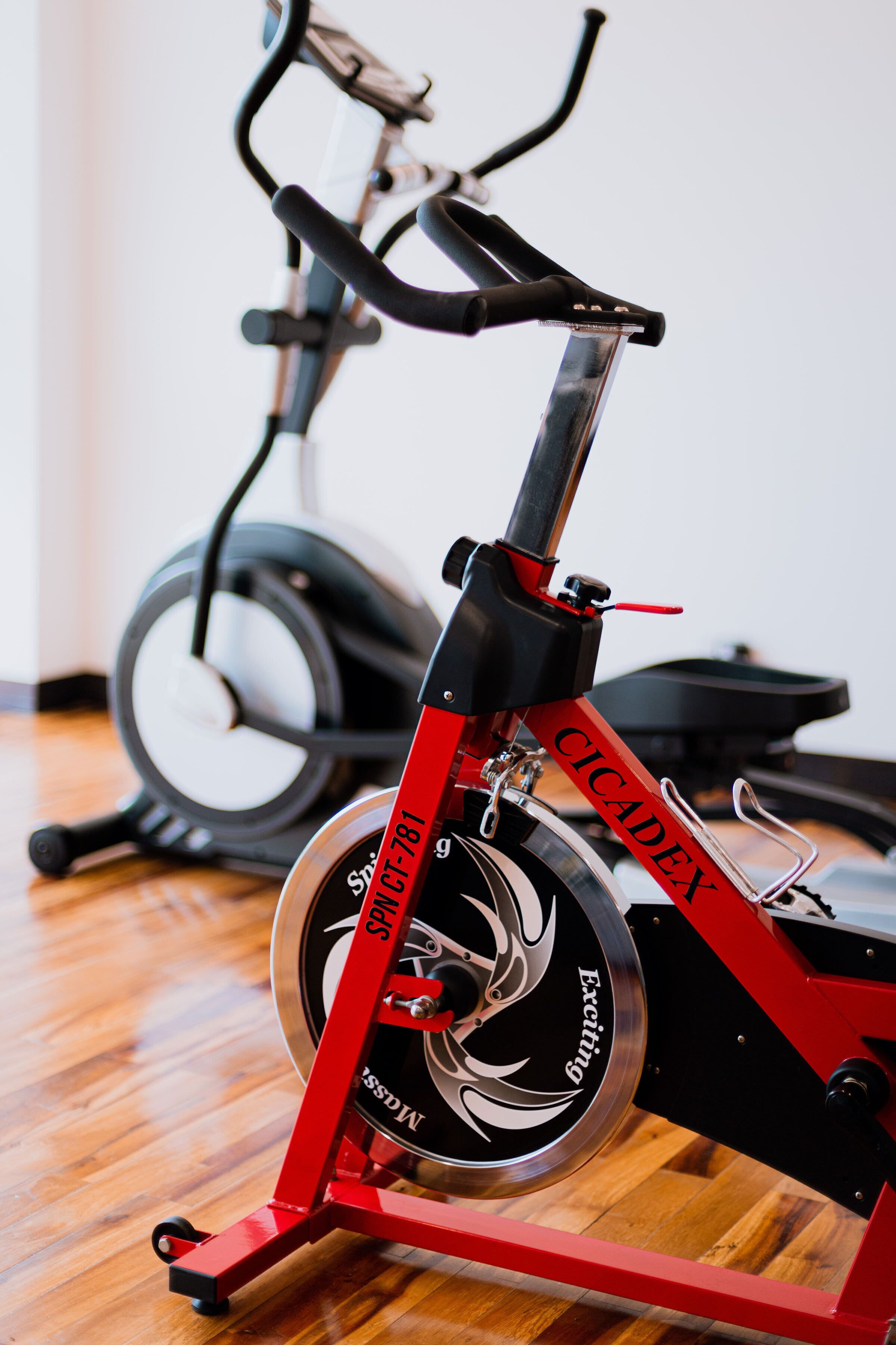 A stationary exercise bike with a red frame and a black seat, positioned on a wooden floor.
