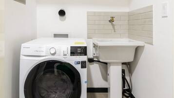 A compact laundry room with a front-loading washing machine, a sink, and a towel rack.