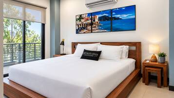 A hotel room with a large bed, a nightstand, a wall-mounted air conditioner, and a window with a view of trees.