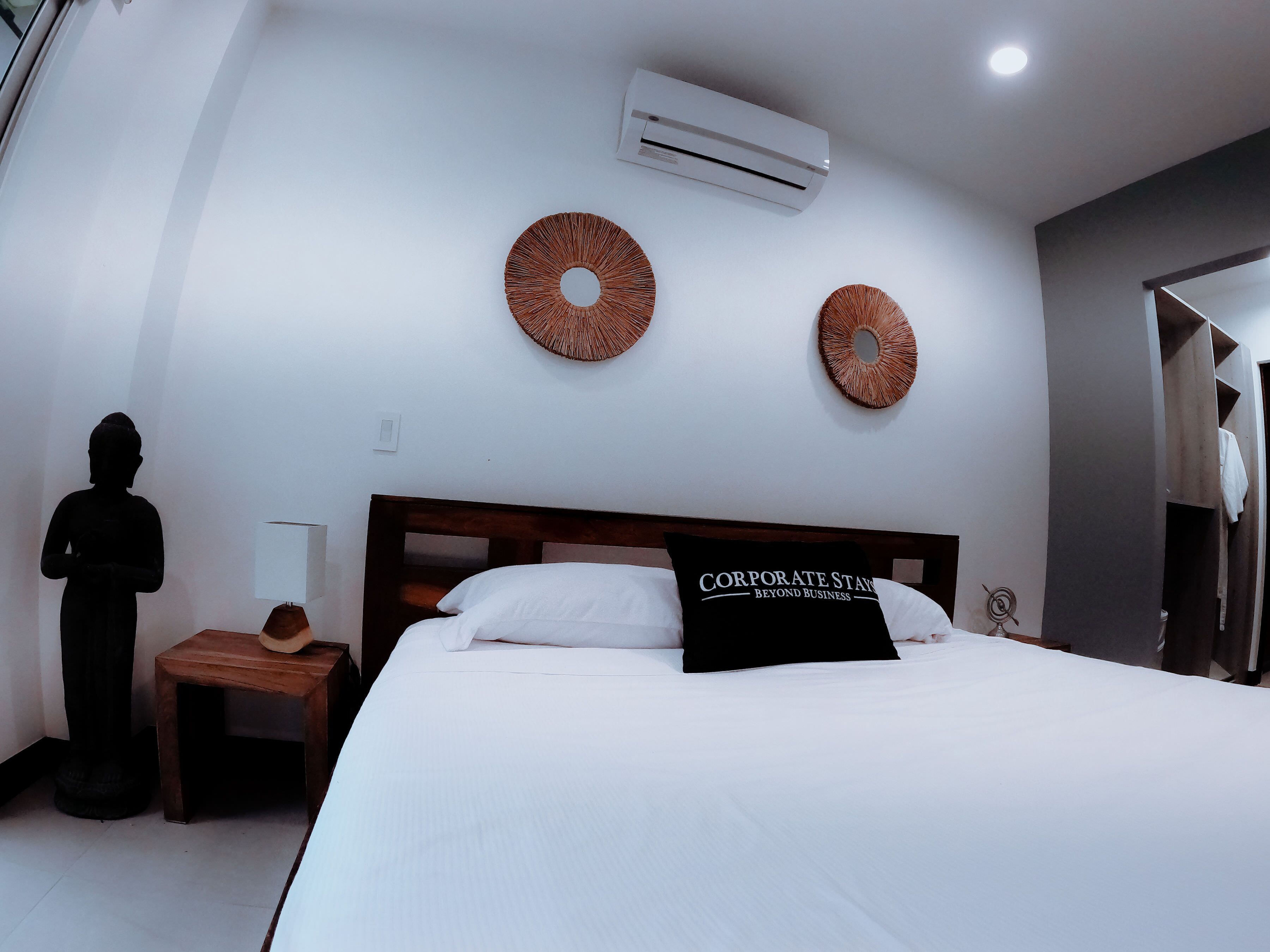Habitación de hotel con cama, mesita de noche, lámpara y aire acondicionado instalado en la pared.