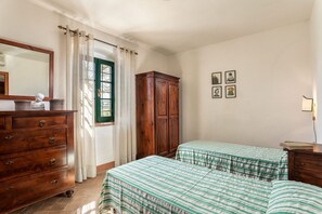 Une chambre avec deux lits, une commode en bois, un miroir et une fenêtre avec des rideaux.