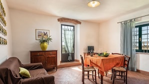 Un coin repas avec une table dressée pour deux personnes, un canapé, un meuble et une fenêtre avec des rideaux.