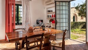 Un coin repas avec une table et des chaises en bois, un rideau rouge et une vue sur un bâtiment en pierre, visible à travers une porte vitrée.