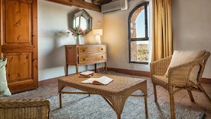 Una habitación acogedora con techo de madera, una mesita de mimbre con un libro, una silla de mimbre, un aparador de madera y una ventana con cortinas.
