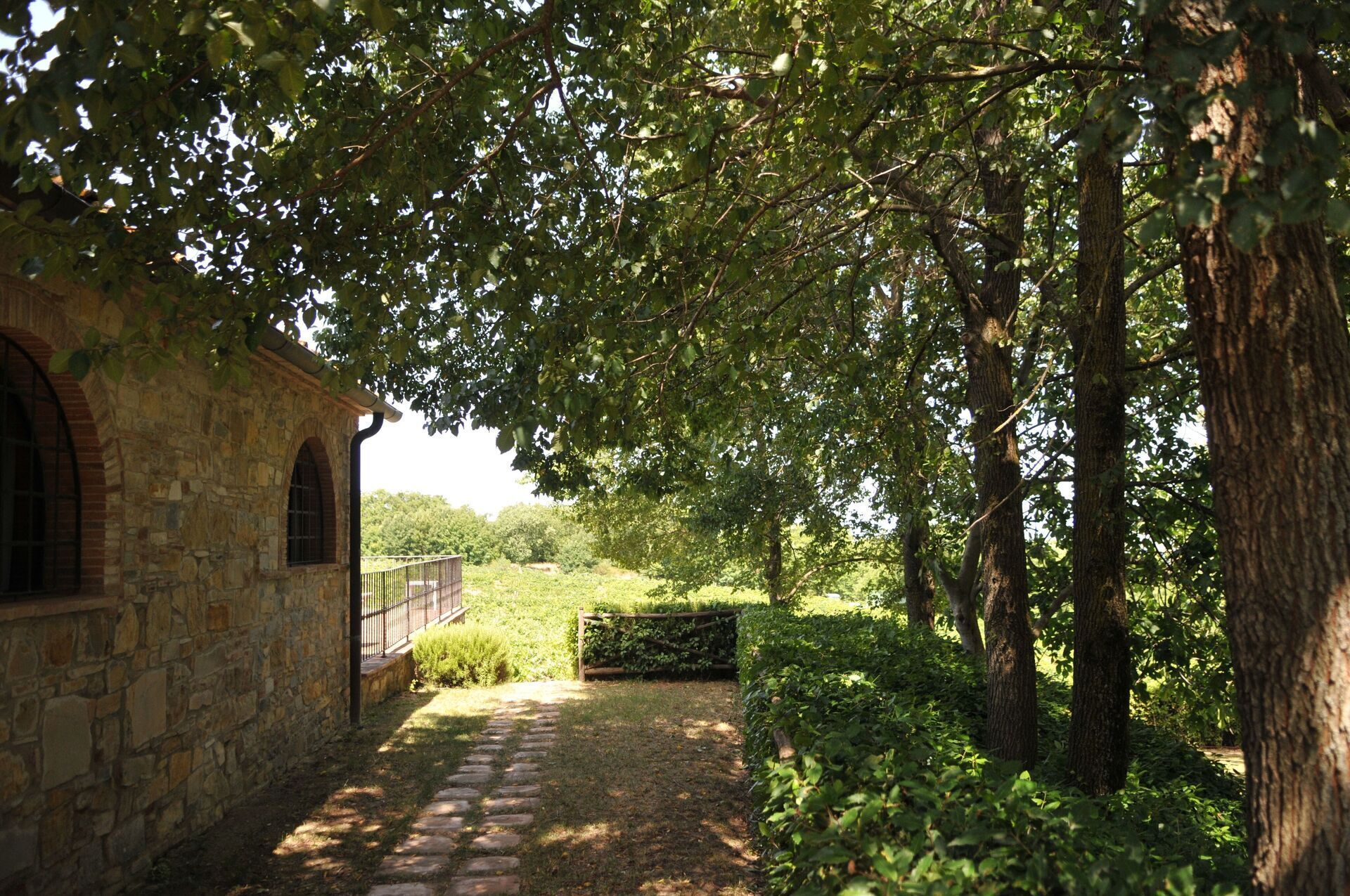 A stone building with arched windows, a stone pathway, and surrounding greenery.