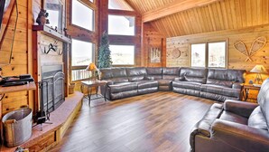A cozy log cabin interior with a large leather sectional sofa, a fireplace, and a view of the outside. - 1 Mi to Granby Ranch: Family-Friendly Cabin! (Granby)