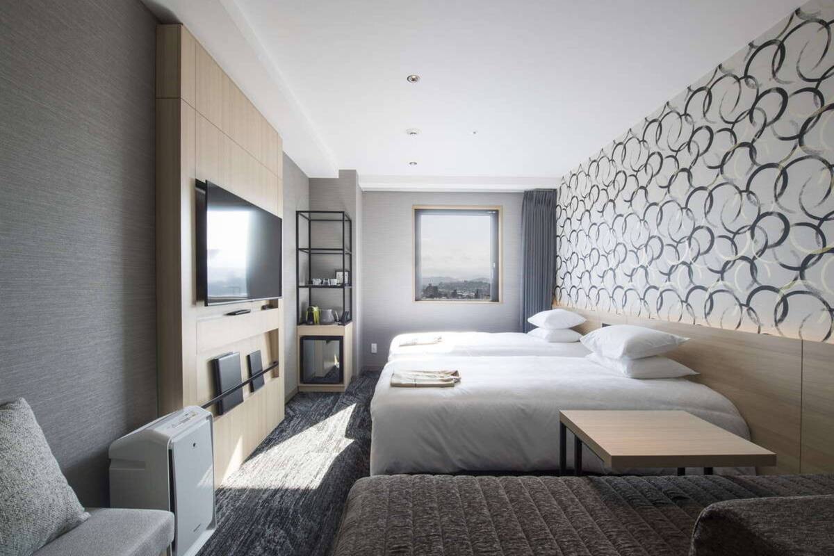 A modern hotel room with a large bed, a desk, a TV, and a city view.