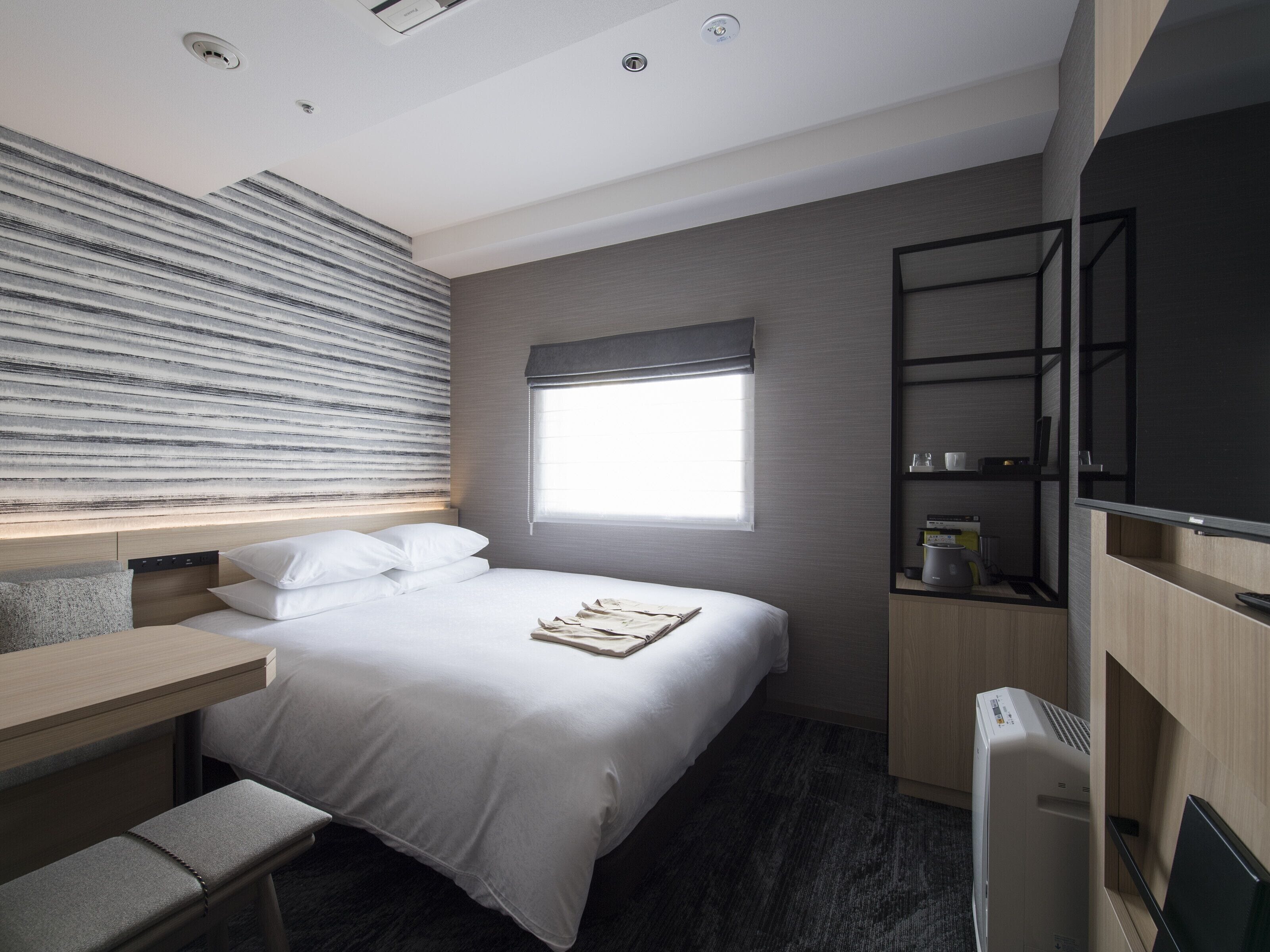 Moderni hotellihuone, jossa on suuri sänky, työpöytä ja seinään upotettu televisio.
