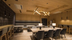 Una sala de conferencias moderna con suelos de madera, mesas y sillas, equipada con luces en el techo y una máquina de hielo visible.