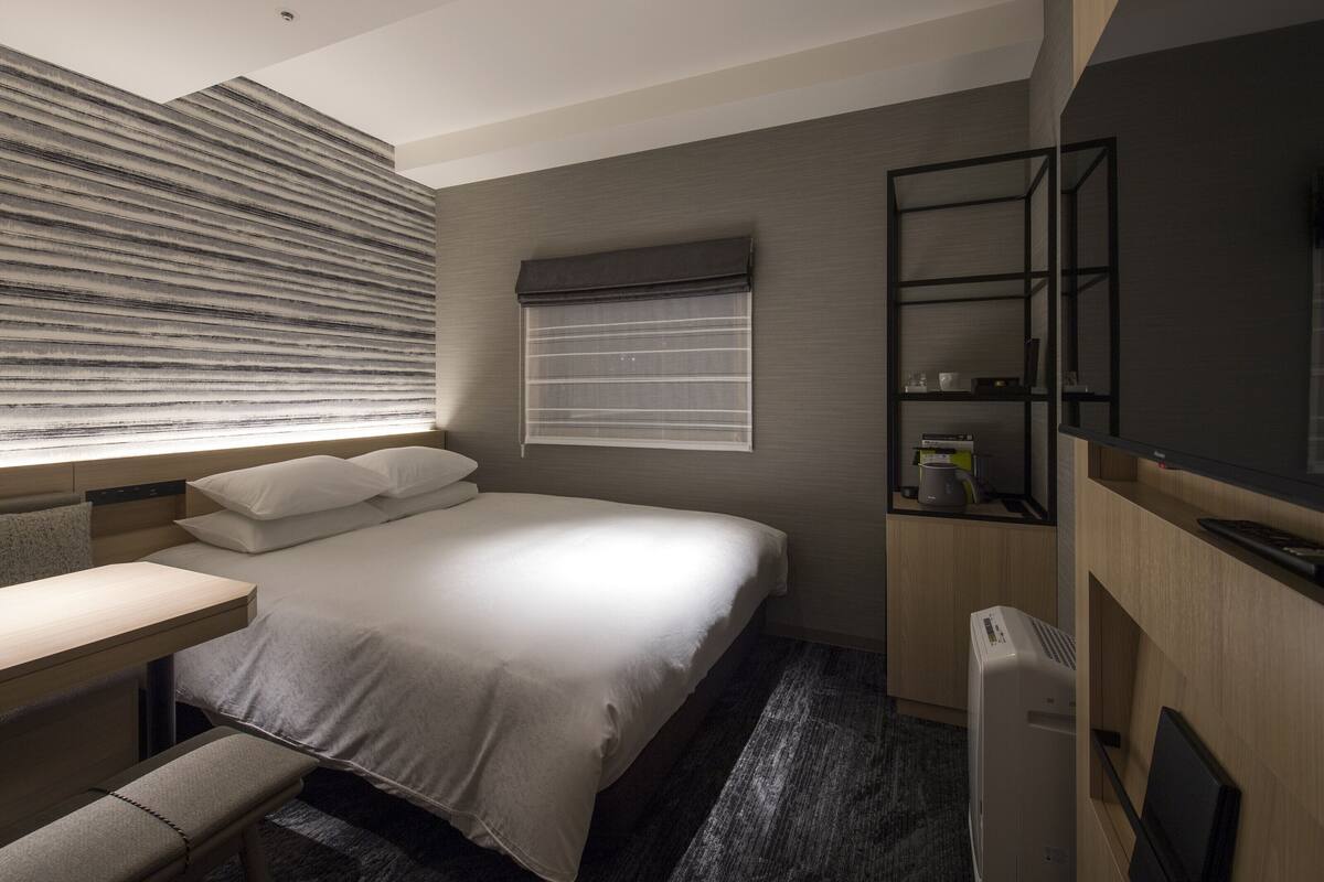 A modern hotel room with a bed, bedside table, and a built-in TV.