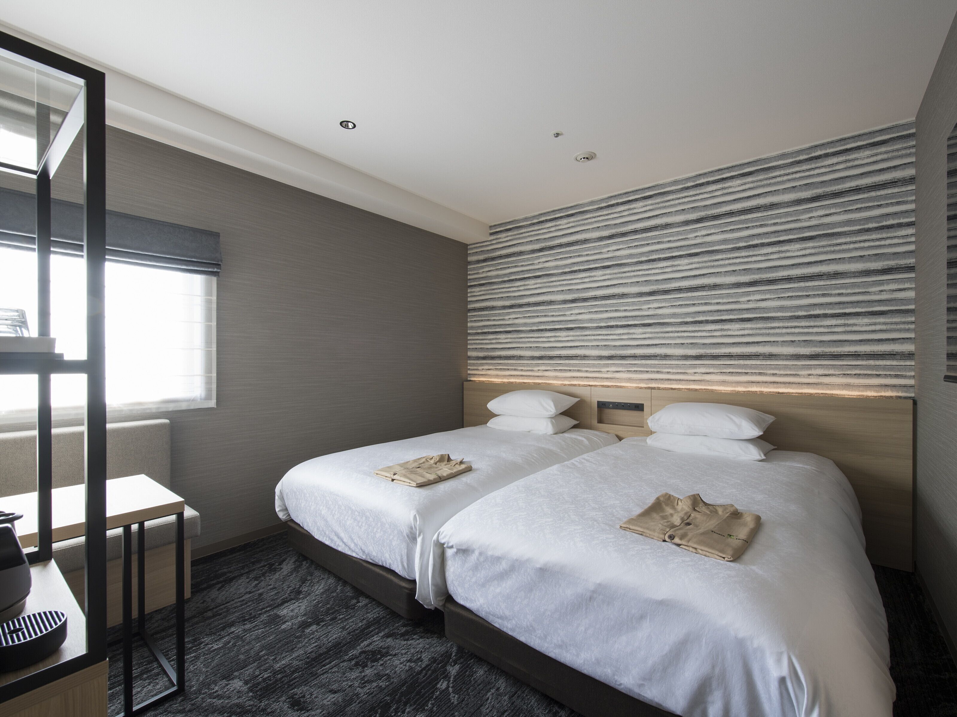 A modern hotel room with two beds, a desk, and a large window.
