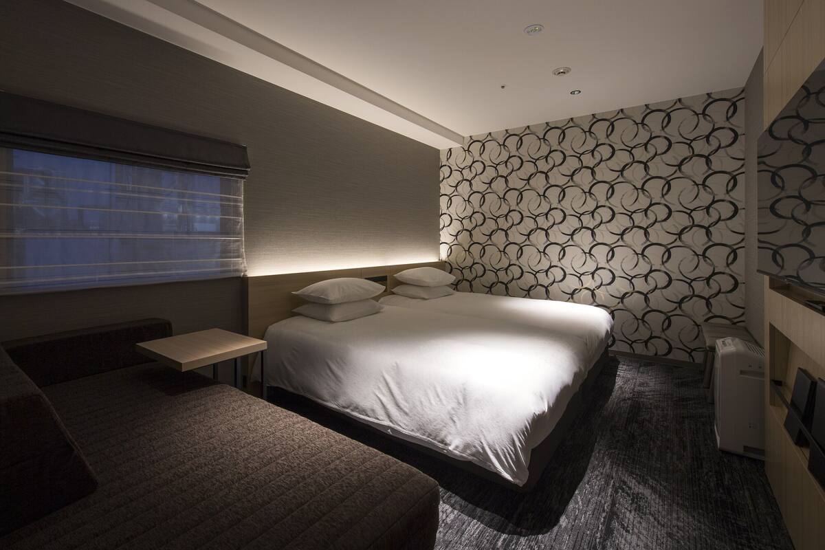 A modern hotel room with a large bed, a bedside table, a small desk, and a patterned wall.