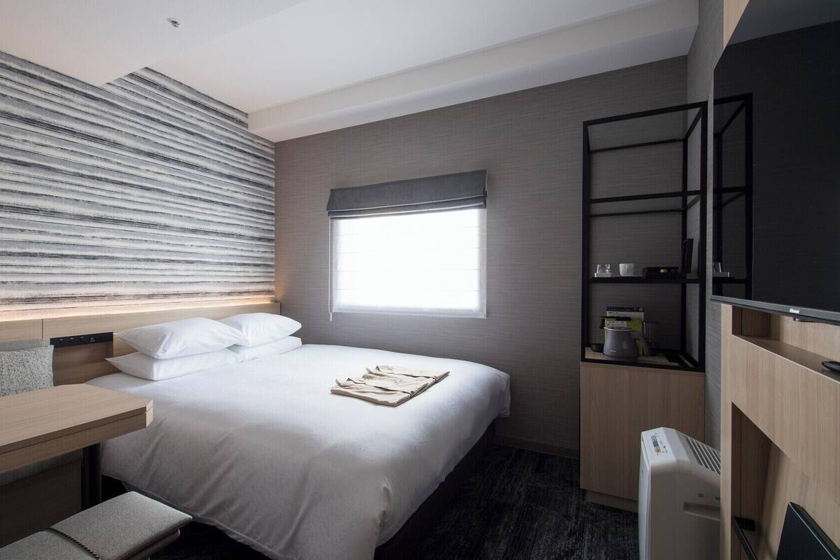 A hotel room with a bed, a desk, a TV, and a window.