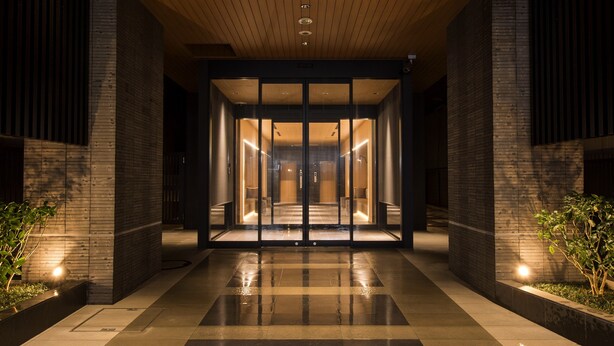 Entrada de un edificio moderno con puertas de vidrio, piso de baldosas y paneles de techo de madera.