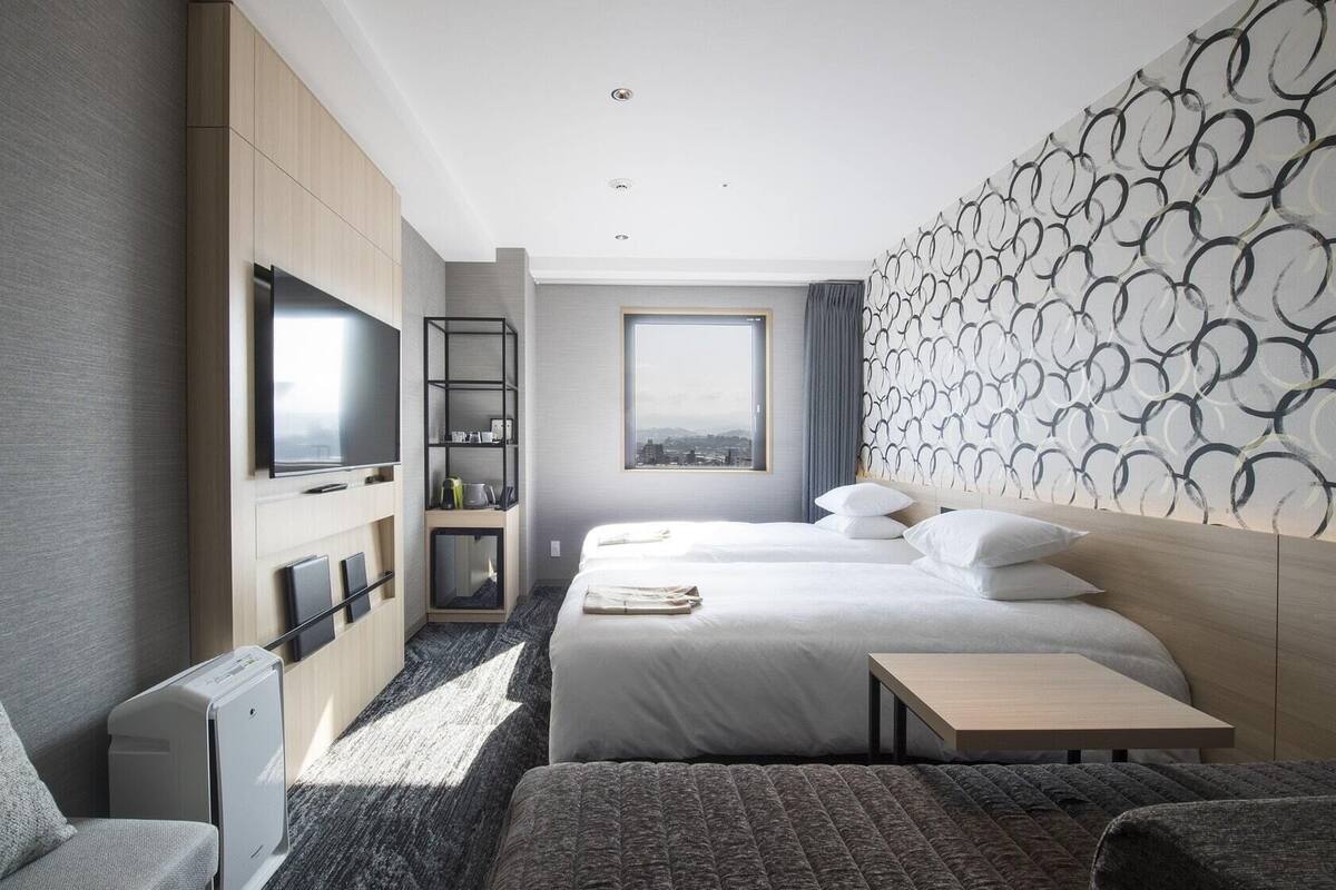 A modern hotel room with a large bed, a desk, a TV, and a city view.