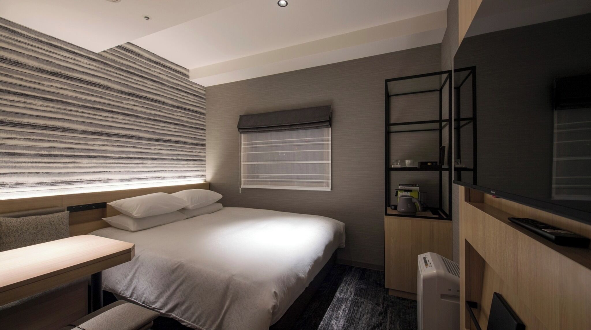 Een moderne hotelkamer met een bed, nachtkastje en een ingebouwde televisie.