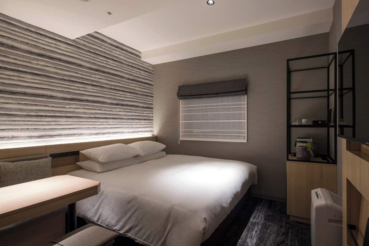Une chambre d’hôtel moderne équipée d’un lit, d’une table de chevet et d’un téléviseur intégré.