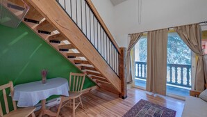 Une pièce avec un escalier en bois, une table entourée de chaises et une vue sur un balcon agrémenté de rideaux.