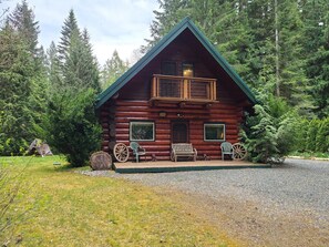 A log cabin with a balcony, two windows, and a porch with two chairs and a bench. - 11SL - Wi-Fi - NO PETS Log Cabin - Sleeps 7 (Deming)