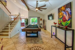 A spacious room with a pool table, a ceiling fan, and a staircase leading to another level.