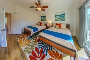 A hotel room with two beds, a ceiling fan, artwork on the walls, and a view of the outdoors.