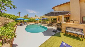 Un patio trasero con piscina, mobiliario de jardín y zona de barbacoa.