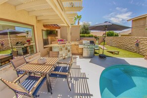 An outdoor patio with a pool, a grill, and a seating area with tables and chairs.