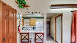 Una cocina con armarios de madera, un refrigerador blanco y dos taburetes de bar.