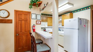 Una cocina con armarios de madera, un refrigerador blanco, una puerta de madera, un extintor y un reloj en la pared.