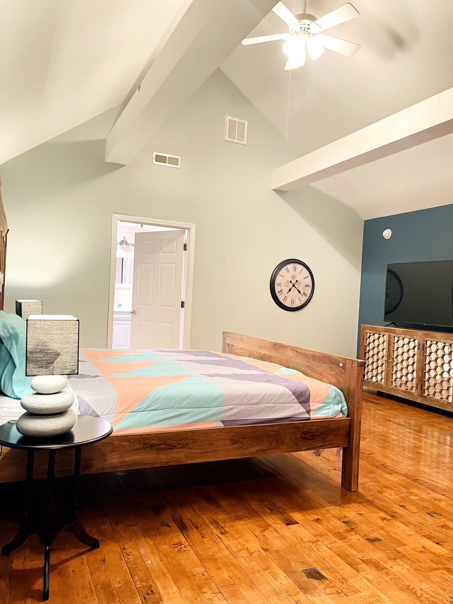 Ein Schlafzimmer mit einem hölzernen Bett, einer Wanduhr, einem Deckenventilator und einer Tür zu einem anderen Raum.