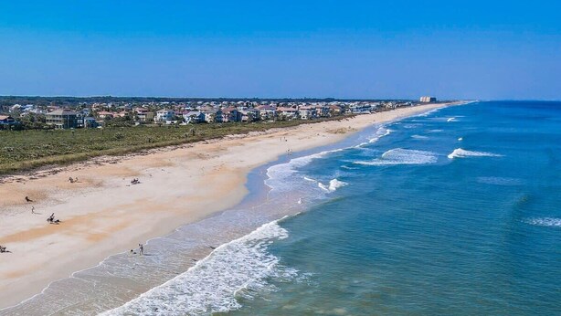 A coastal beach with clear blue waters, sandy shore, and a row of houses along the beach. - 3BR Coastal Home + Heated Pool, Golf Cart & Bikes (Palm Coast)