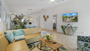 A modern living room with a sofa, coffee table, and a television mounted on the wall. - 3BR Coastal Home + Heated Pool, Golf Cart & Bikes (Palm Coast)