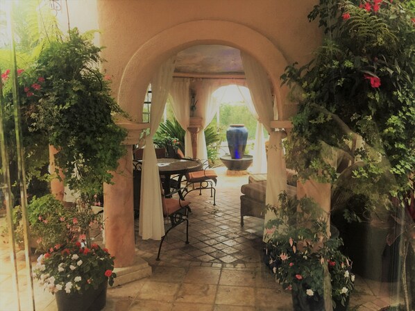 An indoor garden with a table and chairs, surrounded by arches and potted plants.
