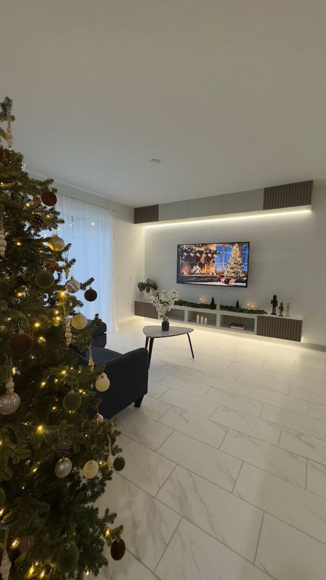 Een moderne woonkamer met een grote flatscreen televisie, een donkere bank en een kerstboom.