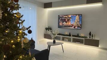 Een moderne woonkamer met een grote flatscreen televisie, een donkere bank en een kerstboom.