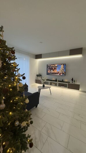 A modern living room with a large flat-screen TV, a dark sofa, and a Christmas tree.