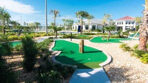 Ein Golfplatz mit Putting Green, Palmen und einem Gebäude im Hintergrund.