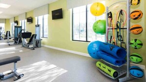 Ein Fitnessraum mit Trainingsgeräten, einem an der Wand montierten Fernseher und großen Fenstern.