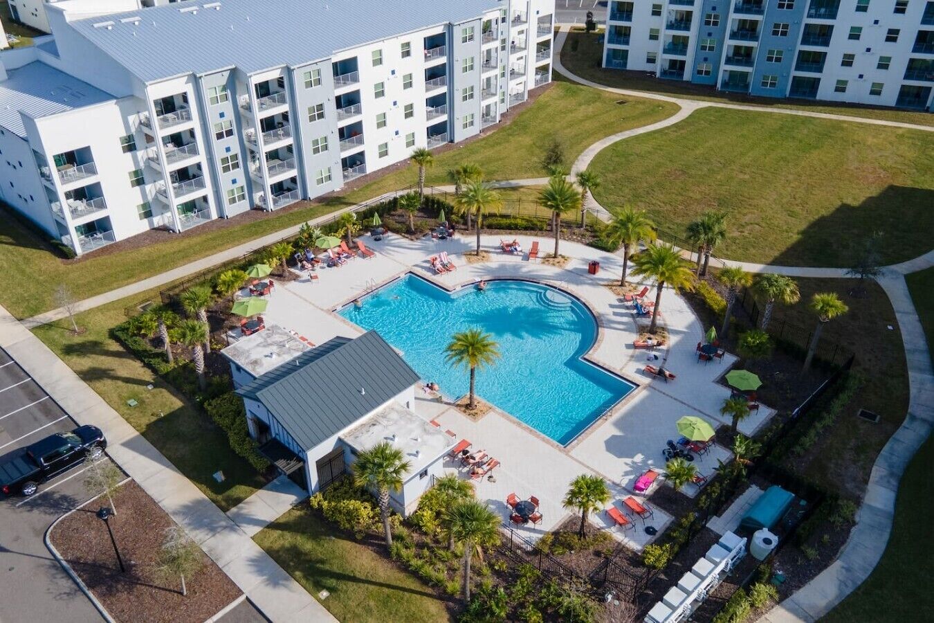Luftaufnahme eines Hotels mit einem zentral gelegenen Swimmingpool, umgeben von Liegestühlen und Palmen.