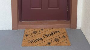 A brown door with a wreath and a doormat with 'Merry Christmas' written on it.