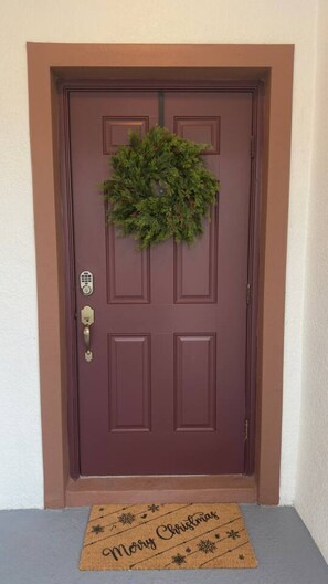 Puerta marrón con un adorno navideño y felpudo con la leyenda 'Merry Christmas'.